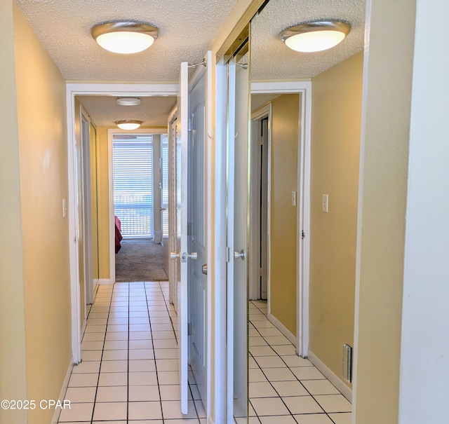 hallway featuring light tile patterned flooring, a textured ceiling, and baseboards