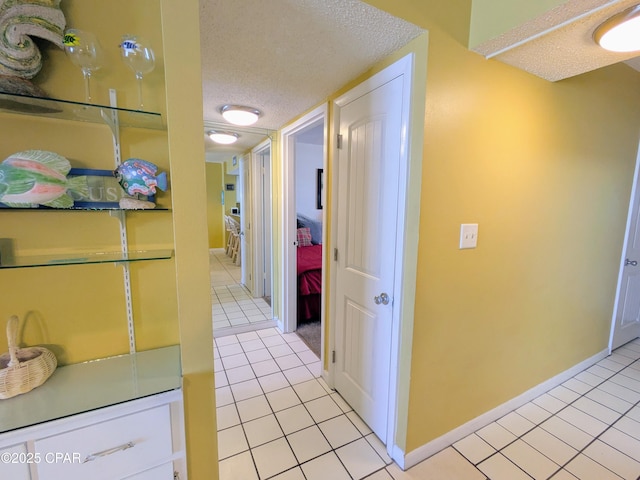 hallway featuring light tile patterned flooring, a textured ceiling, and baseboards