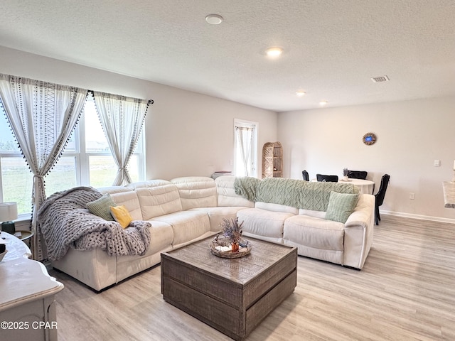 living area with light wood finished floors, visible vents, and a textured ceiling