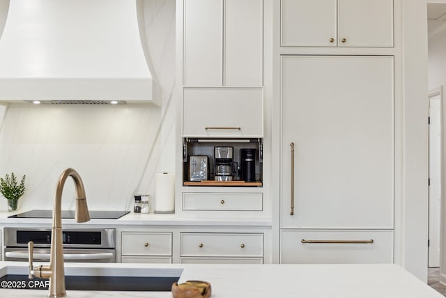 kitchen with black electric cooktop, stainless steel oven, white cabinets, and light countertops