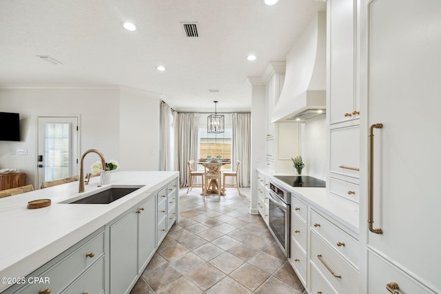 kitchen with custom range hood, visible vents, a healthy amount of sunlight, stainless steel oven, and a sink