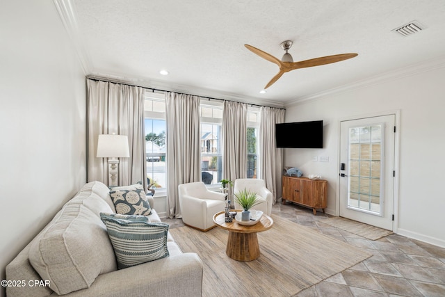 living room with visible vents, ornamental molding, a ceiling fan, a textured ceiling, and baseboards