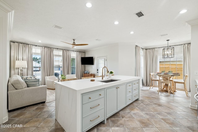 kitchen with ornamental molding, open floor plan, a kitchen island with sink, light countertops, and a sink