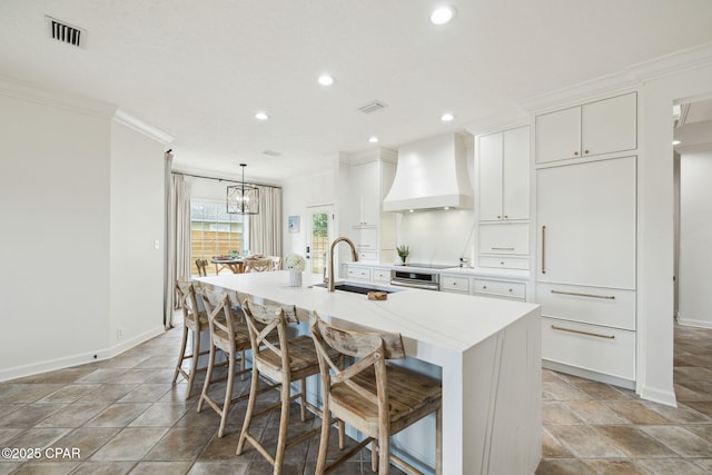 kitchen featuring a sink, visible vents, ornamental molding, custom exhaust hood, and an island with sink