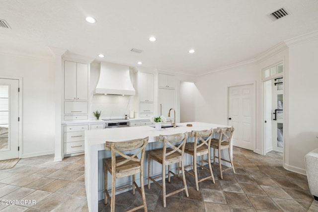 kitchen with ornamental molding, a kitchen island with sink, visible vents, and custom exhaust hood