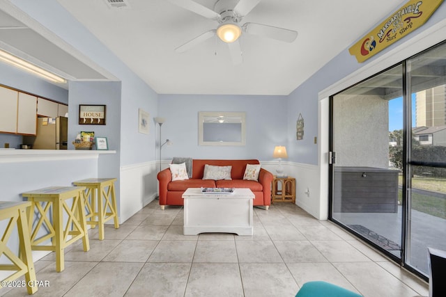 living area with light tile patterned floors, visible vents, wainscoting, and ceiling fan