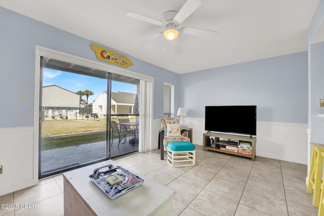 living area featuring light tile patterned floors, a wainscoted wall, and ceiling fan