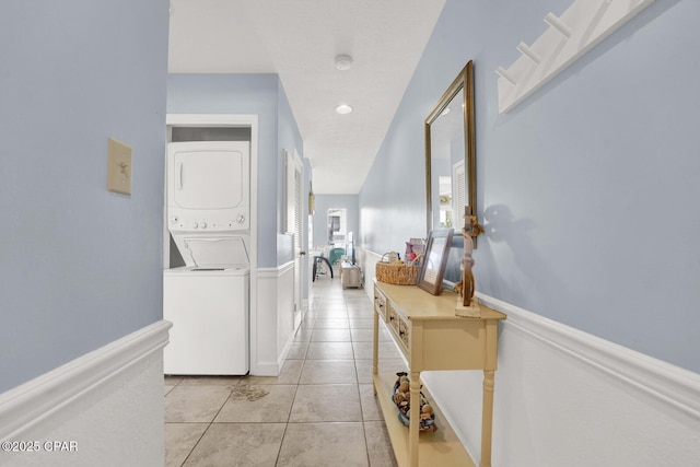 hall with light tile patterned floors, stacked washer and clothes dryer, and wainscoting