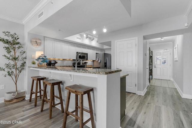 kitchen featuring a peninsula, visible vents, light wood-style floors, appliances with stainless steel finishes, and crown molding