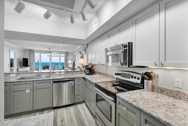 kitchen featuring stainless steel appliances, a sink, ornamental molding, gray cabinets, and light wood finished floors