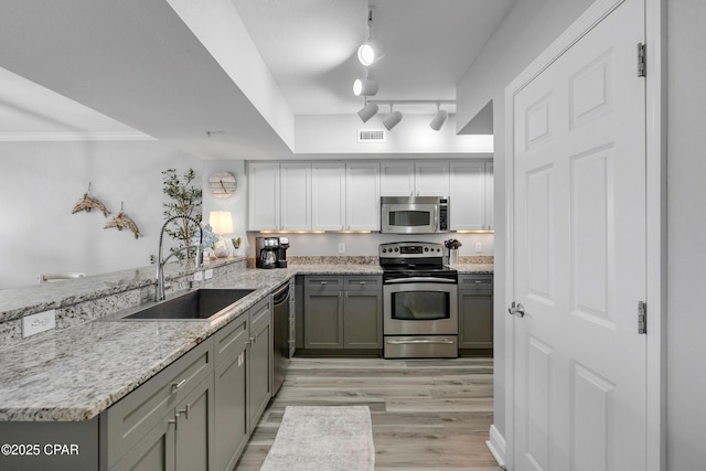 kitchen with appliances with stainless steel finishes, a peninsula, light stone countertops, light wood-type flooring, and a sink