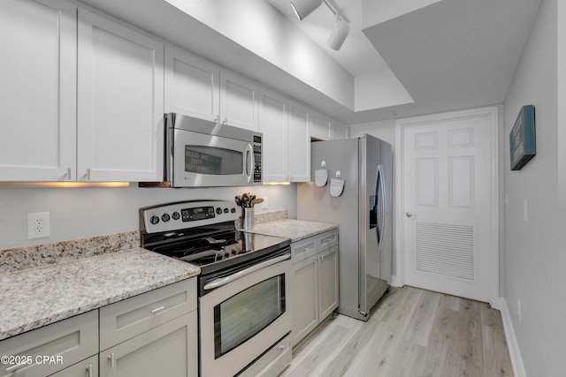 kitchen featuring stainless steel appliances, rail lighting, light stone countertops, light wood-type flooring, and baseboards