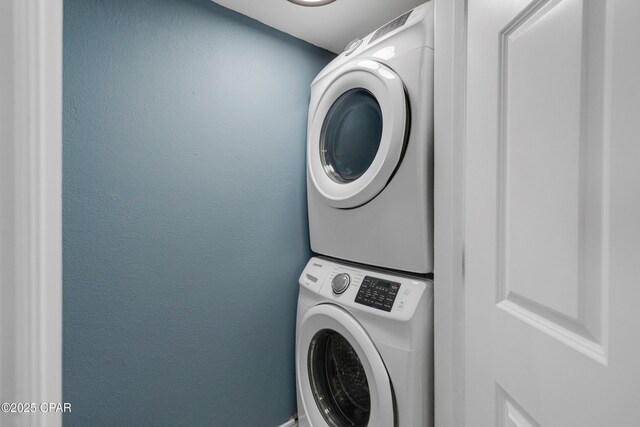 laundry room with a textured wall, laundry area, and stacked washer / dryer