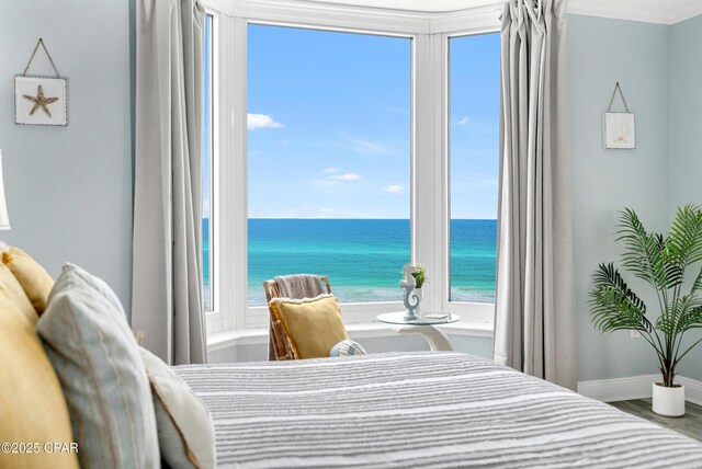 bedroom featuring ornamental molding, a water view, baseboards, and wood finished floors