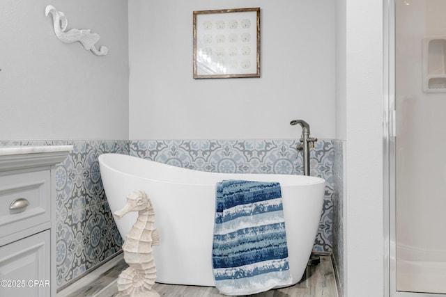 full bath with a soaking tub, wainscoting, and wood finished floors