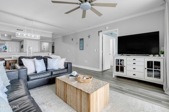 living area with visible vents, a ceiling fan, baseboards, ornamental molding, and light wood finished floors