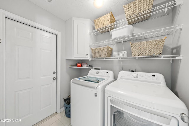 laundry area featuring a textured ceiling, separate washer and dryer, light tile patterned flooring, and cabinet space