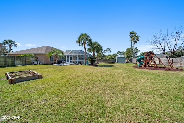 view of yard with a garden, glass enclosure, a fenced backyard, a shed, and a playground