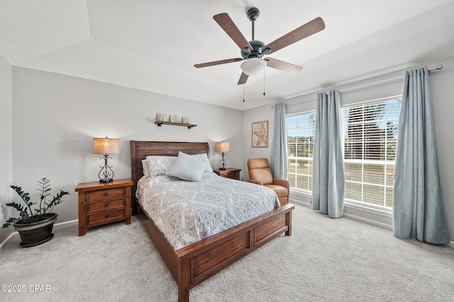 carpeted bedroom with a raised ceiling, a ceiling fan, and baseboards