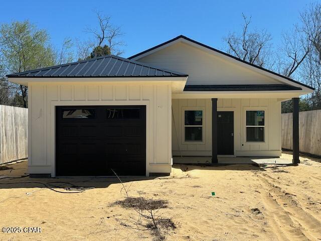 view of front of home with a garage, metal roof, board and batten siding, and fence