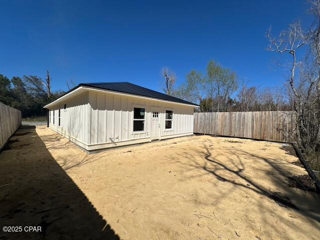 rear view of house featuring a standing seam roof, metal roof, board and batten siding, and a fenced backyard