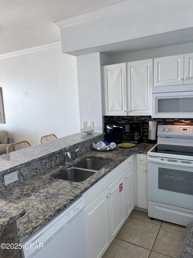 kitchen featuring dark stone counters, a sink, light tile patterned floors, white appliances, and white cabinets