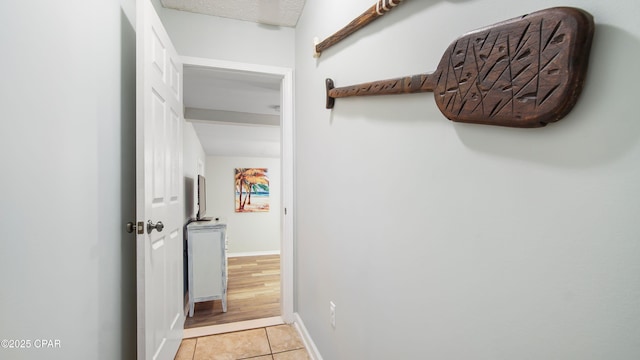 hallway featuring light tile patterned floors, baseboards, and a textured ceiling