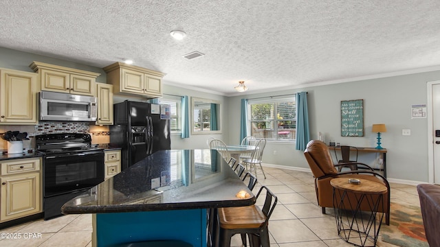 kitchen with a breakfast bar, visible vents, cream cabinets, light tile patterned flooring, and black appliances