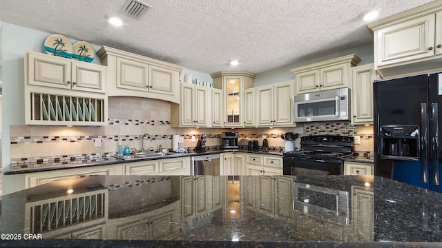 kitchen featuring visible vents, backsplash, cream cabinetry, black appliances, and a sink