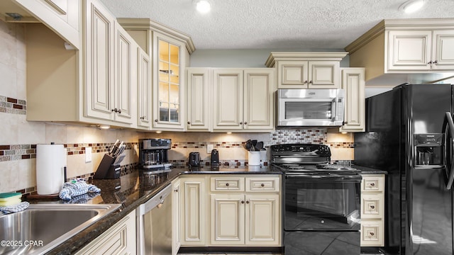 kitchen featuring cream cabinetry, backsplash, dark stone counters, black appliances, and glass insert cabinets