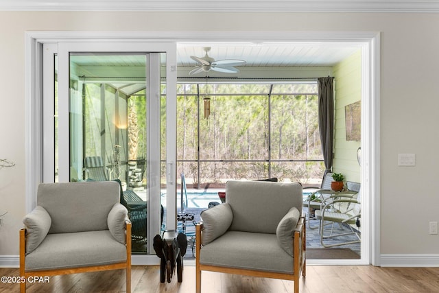 sitting room with baseboards, crown molding, a ceiling fan, and wood finished floors