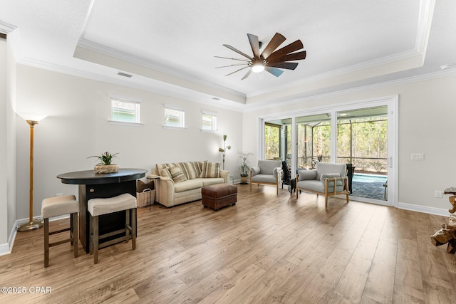 living room with light wood-style floors, a tray ceiling, a healthy amount of sunlight, and visible vents