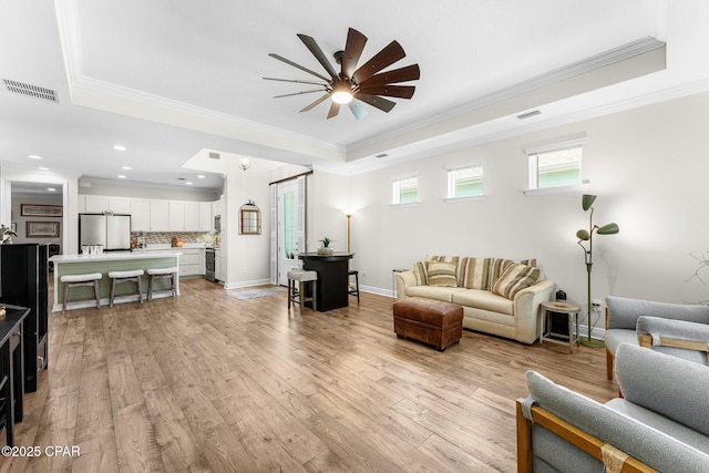 living room with a tray ceiling, light wood-style flooring, and visible vents