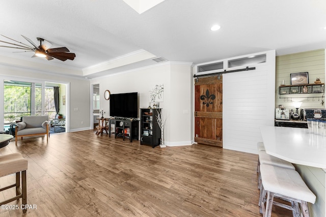 living room featuring a barn door, visible vents, ceiling fan, wood finished floors, and crown molding