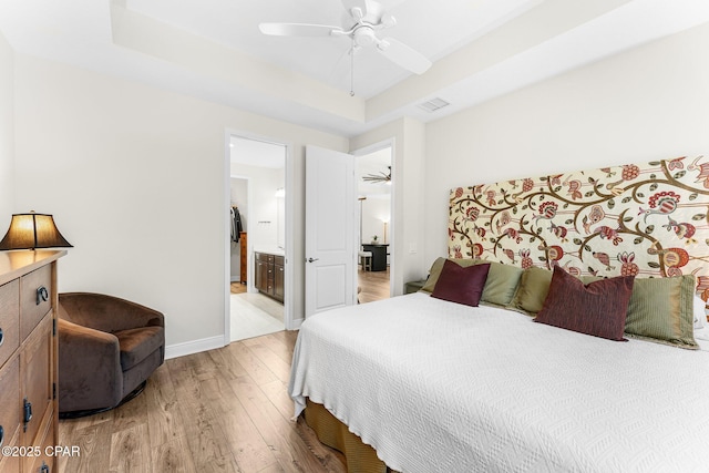 bedroom with ensuite bathroom, visible vents, baseboards, light wood-type flooring, and a tray ceiling