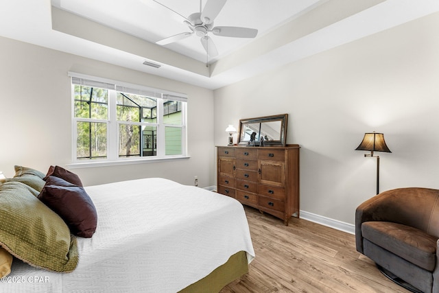 bedroom with a raised ceiling, visible vents, light wood-style floors, ceiling fan, and baseboards