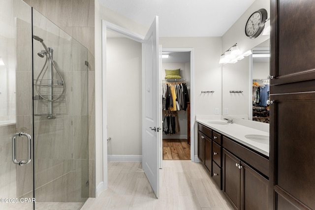 full bath with a sink, baseboards, a spacious closet, a shower stall, and double vanity