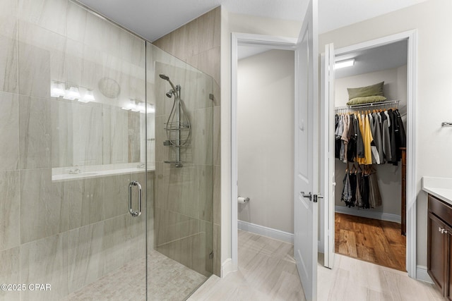 full bath featuring a spacious closet, a stall shower, vanity, and baseboards