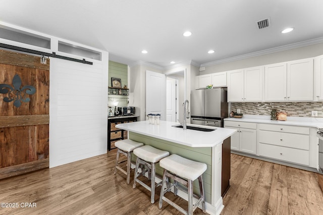 kitchen with a barn door, a kitchen breakfast bar, freestanding refrigerator, light wood-type flooring, and a sink