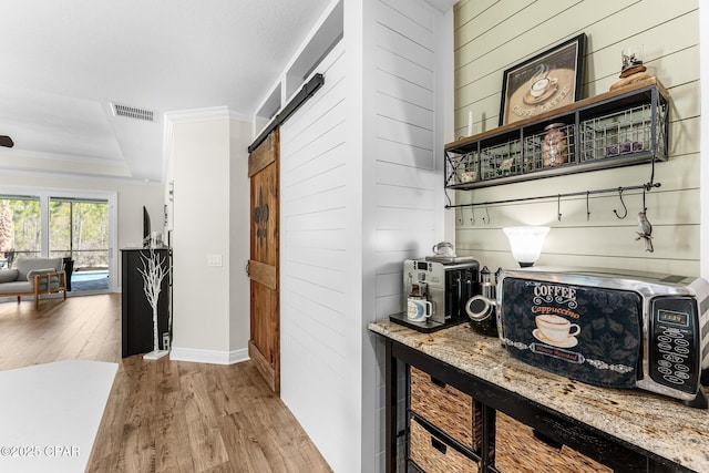 bar with a barn door, visible vents, wood finished floors, a tray ceiling, and crown molding