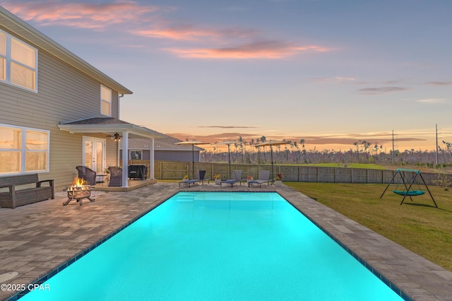 pool at dusk with a yard, a patio, a fire pit, and a fenced backyard