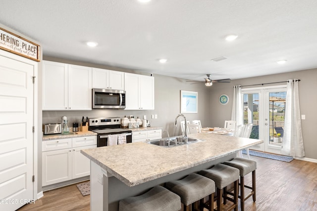 kitchen with a kitchen bar, light wood-style flooring, white cabinets, stainless steel appliances, and a sink