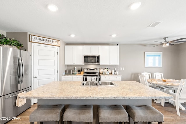 kitchen with visible vents, a kitchen bar, light wood-style flooring, white cabinets, and stainless steel appliances