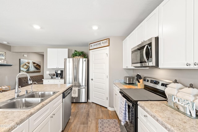 kitchen with light countertops, light wood-style flooring, white cabinets, stainless steel appliances, and a sink