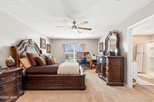 bedroom featuring light carpet, connected bathroom, a textured ceiling, and ceiling fan