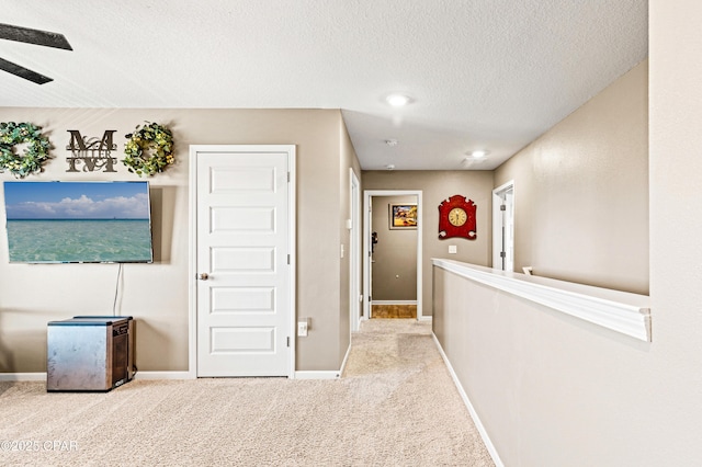 hall featuring baseboards, carpet floors, and a textured ceiling