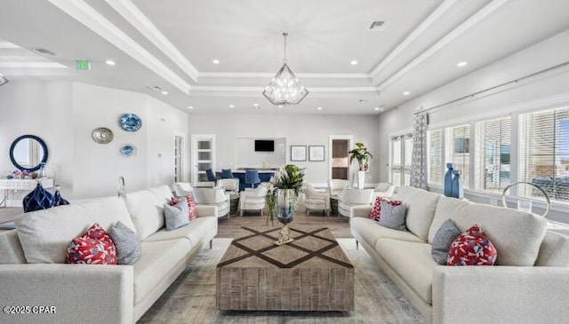 living room featuring a tray ceiling, a notable chandelier, crown molding, recessed lighting, and wood finished floors