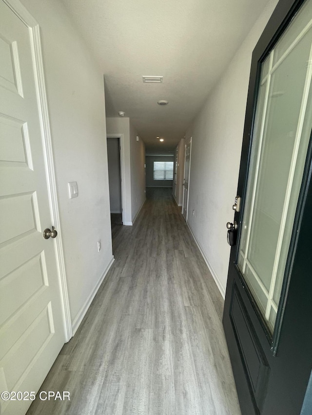 hall featuring baseboards, visible vents, and wood finished floors