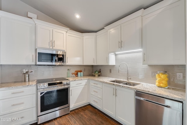 kitchen featuring tasteful backsplash, white cabinets, vaulted ceiling, stainless steel appliances, and a sink