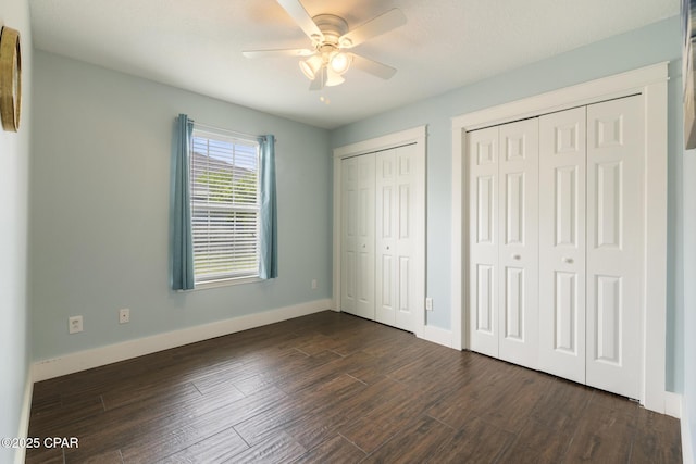 unfurnished bedroom with dark wood-type flooring, ceiling fan, baseboards, and two closets